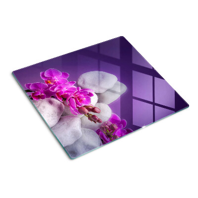 Tabla de cortar de cristal Flores de orquídea sobre un fondo de piedras.