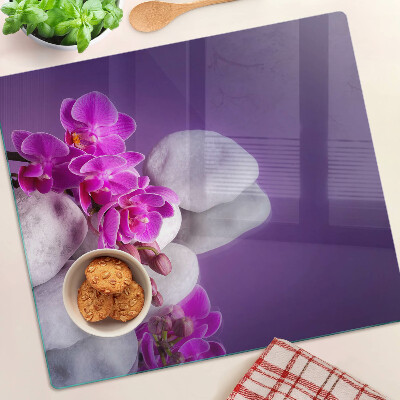 Tabla de cortar de cristal Flores de orquídea sobre un fondo de piedras.