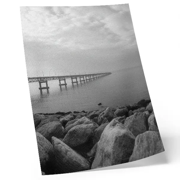 Póster de paisaje tranquilo con puente en playa rocosa bajo cielo gris y colores saturados