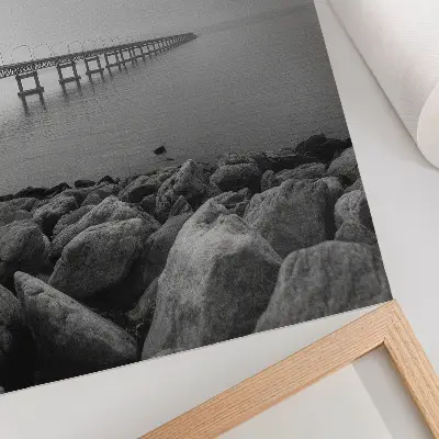 Póster de paisaje tranquilo con puente en playa rocosa bajo cielo gris y colores saturados