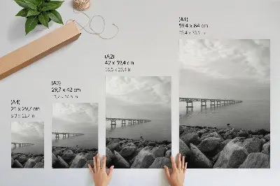 Póster de paisaje tranquilo con puente en playa rocosa bajo cielo gris y colores saturados
